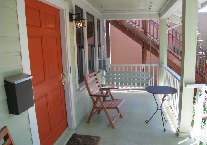 A cozy porch with a red door, a swing, a chair, and a small table.