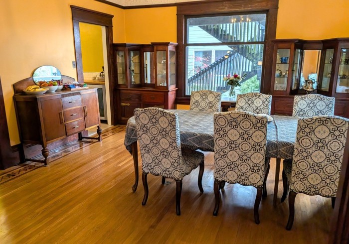 A dining room with a table and chairs, wooden floor, yellow walls, and a wooden hutch.