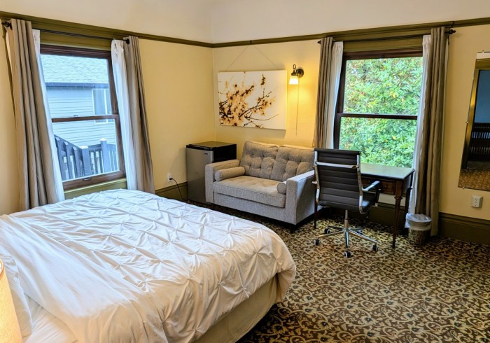A hotel room with a bed, sofa, desk, and window.