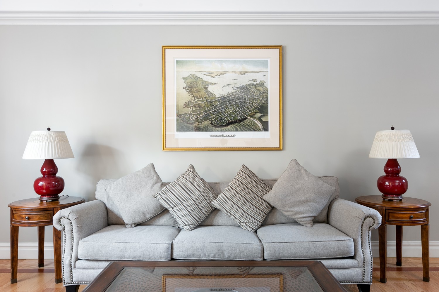 A light gray couch with pillows sits in a lobby with a coffee table and end tables with lamps on either side, under a framed map.