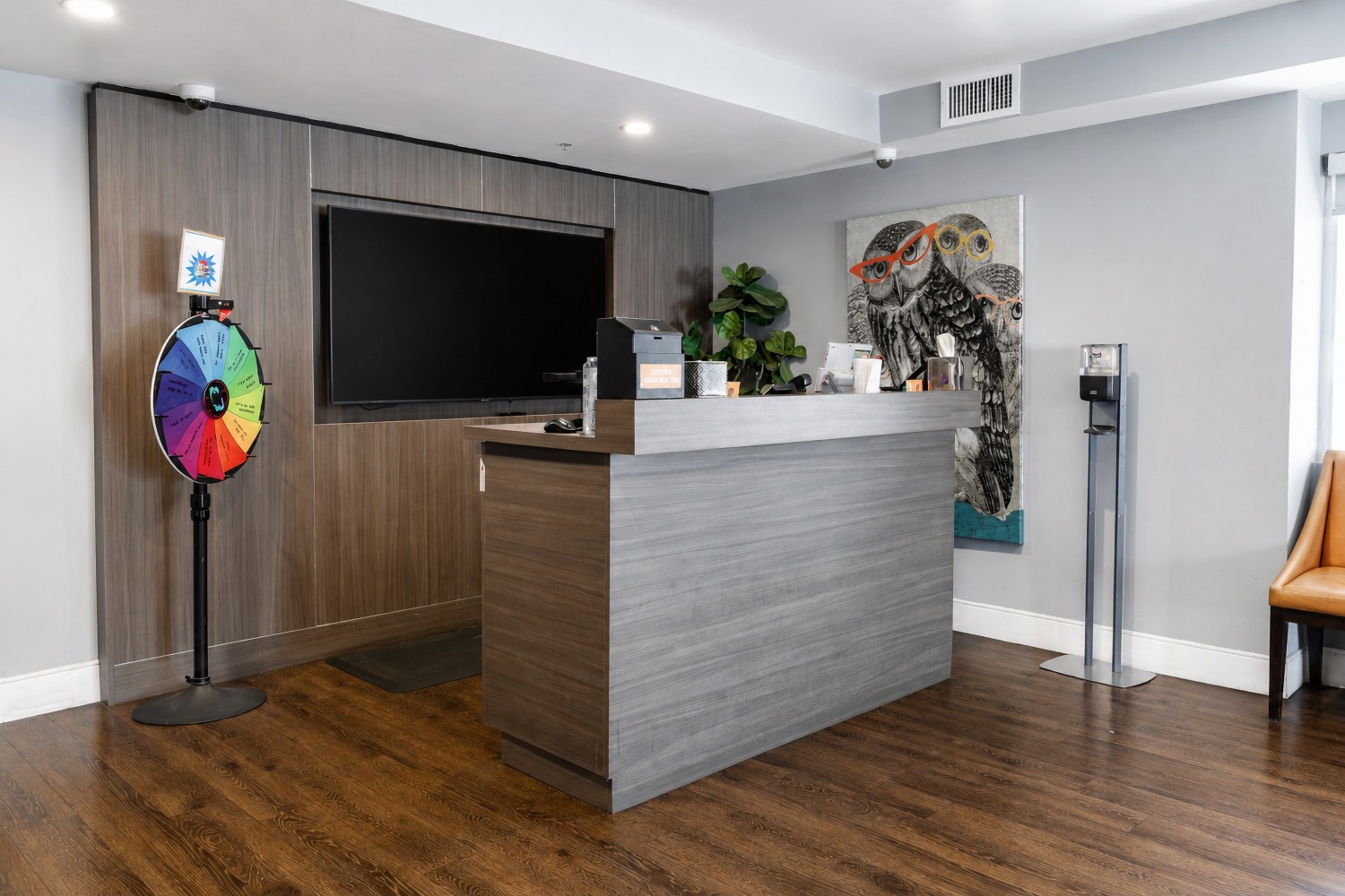 A hotel lobby with a reception desk, TV, prize wheel, and artwork.
